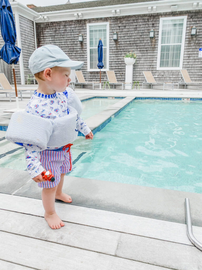 A child stands near a pool while wearing a life jacket