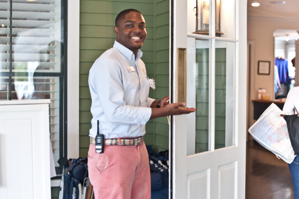 A man stands in front of an open door in a welcoming fashion