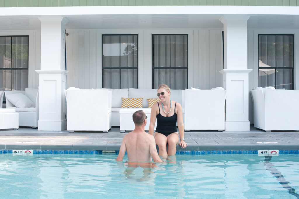 A man standing in a pool while speaking to a woman sitting nearby