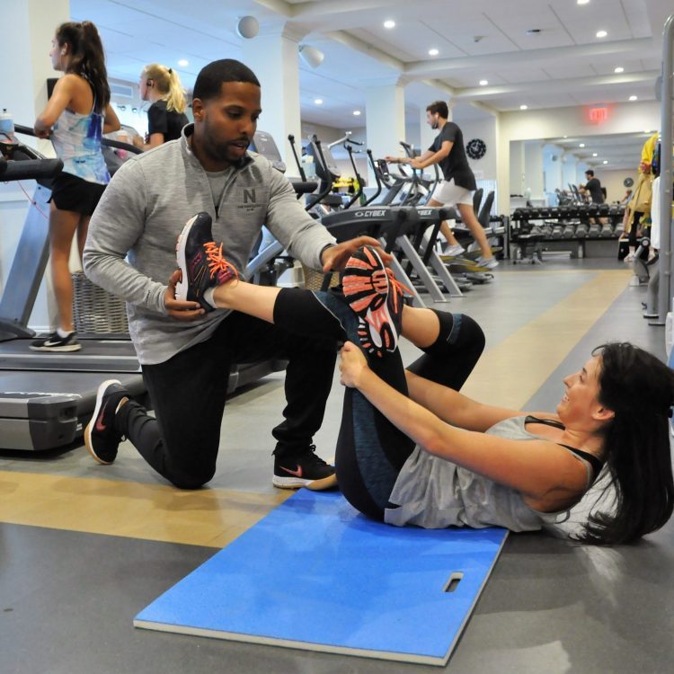 A trainer helps out a fitness student with some stretches